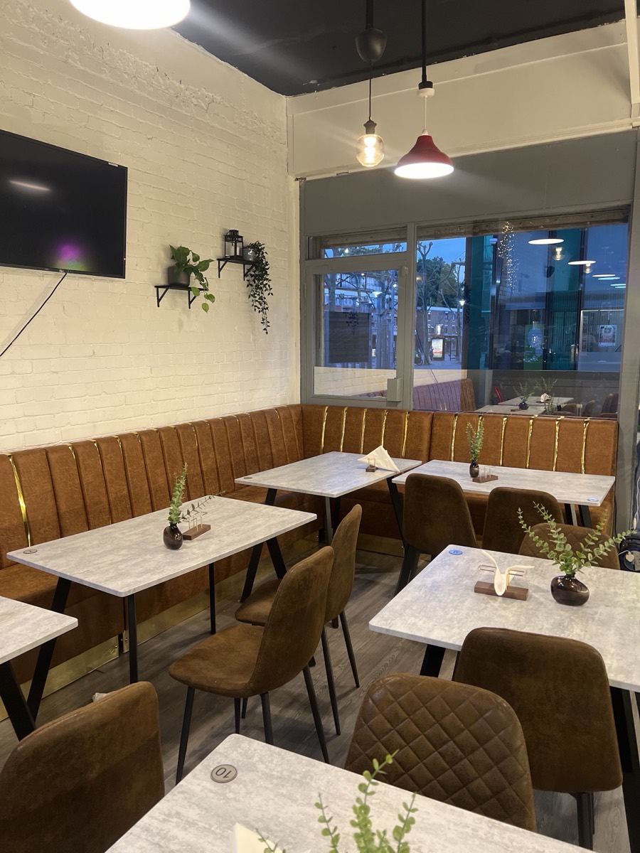 Inside Nafsoor — cognac leather banquette seating with gold trim, marble tables and warm pendant lighting against white brick